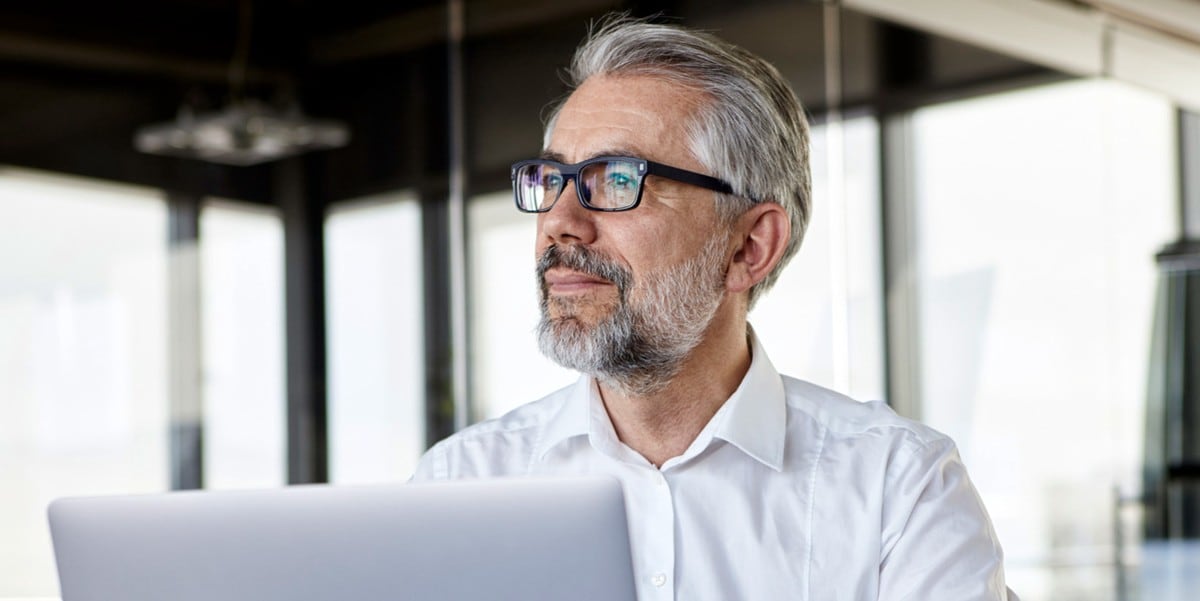 professional man smiling, in the office, laptop in front of him