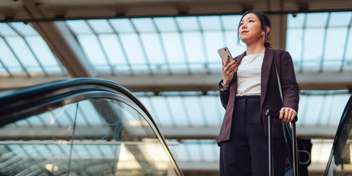 traveler at airport, using escalator, phone in hand
