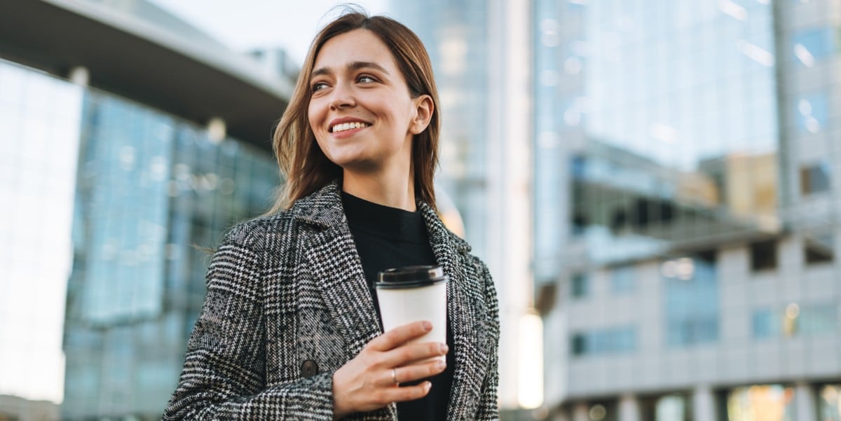 woman standing in front of office building, coffee cup in hand