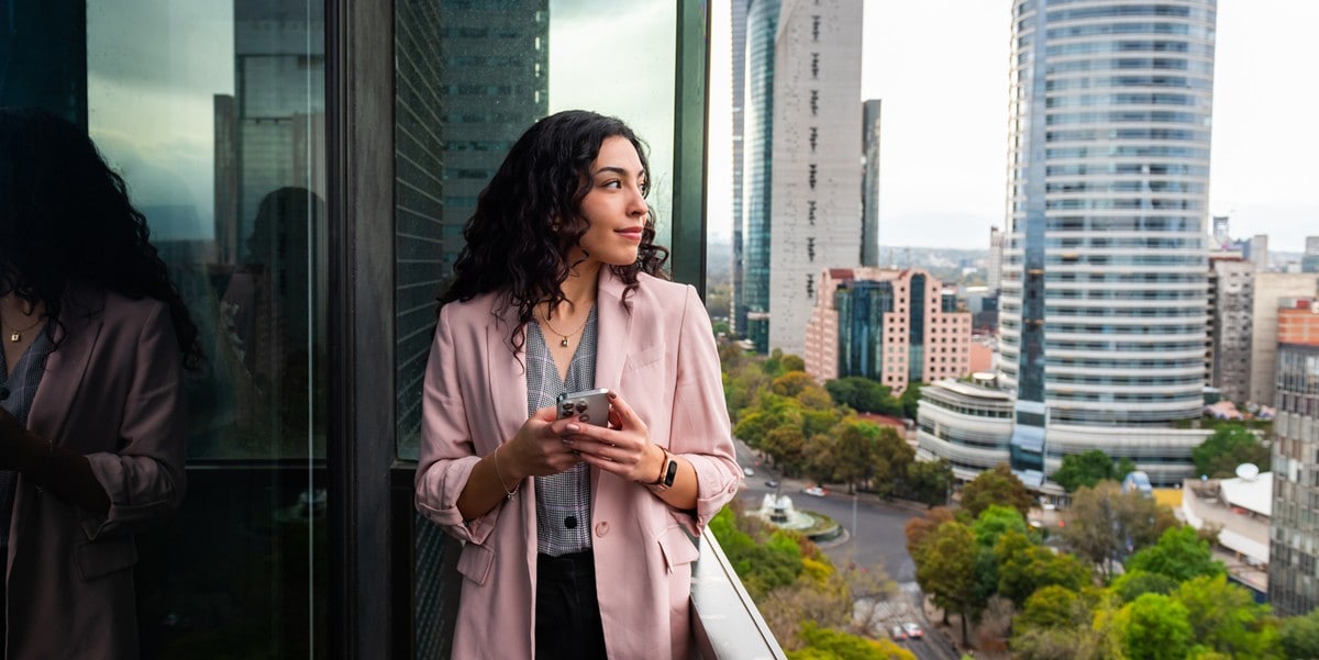 professional woman standing outside on balcony, holding cell phone