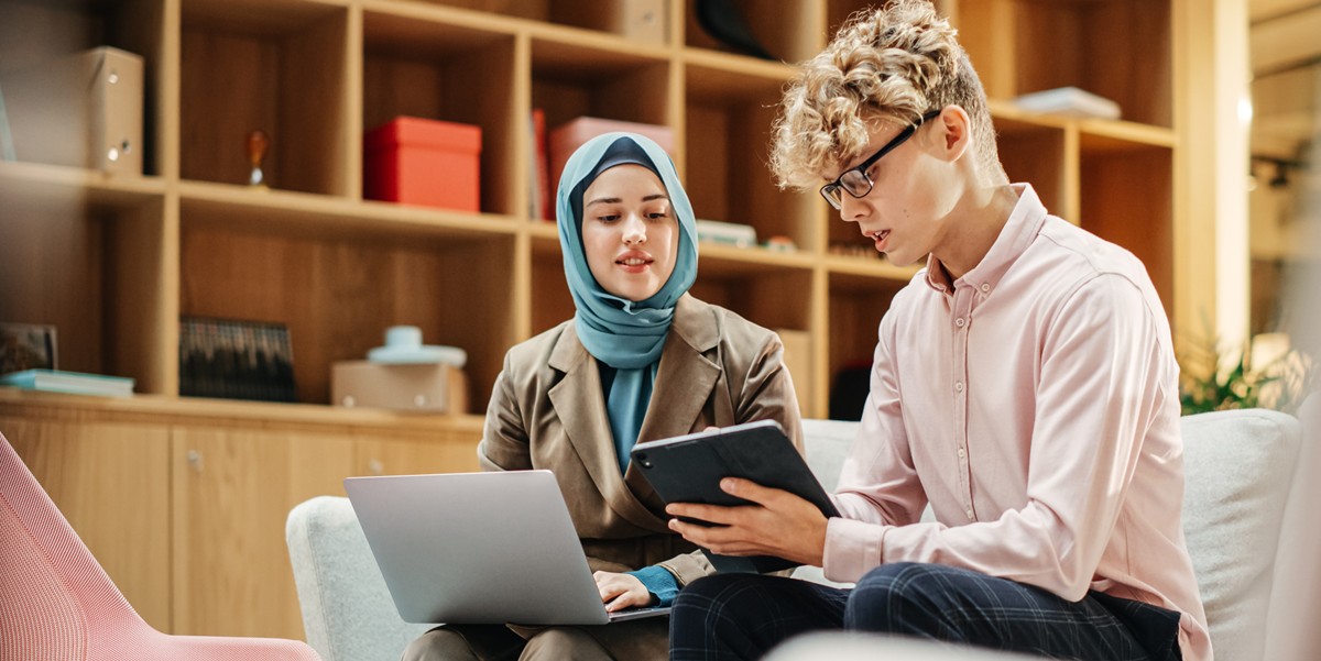 two professionals sitting at a sofa, looking at laptops