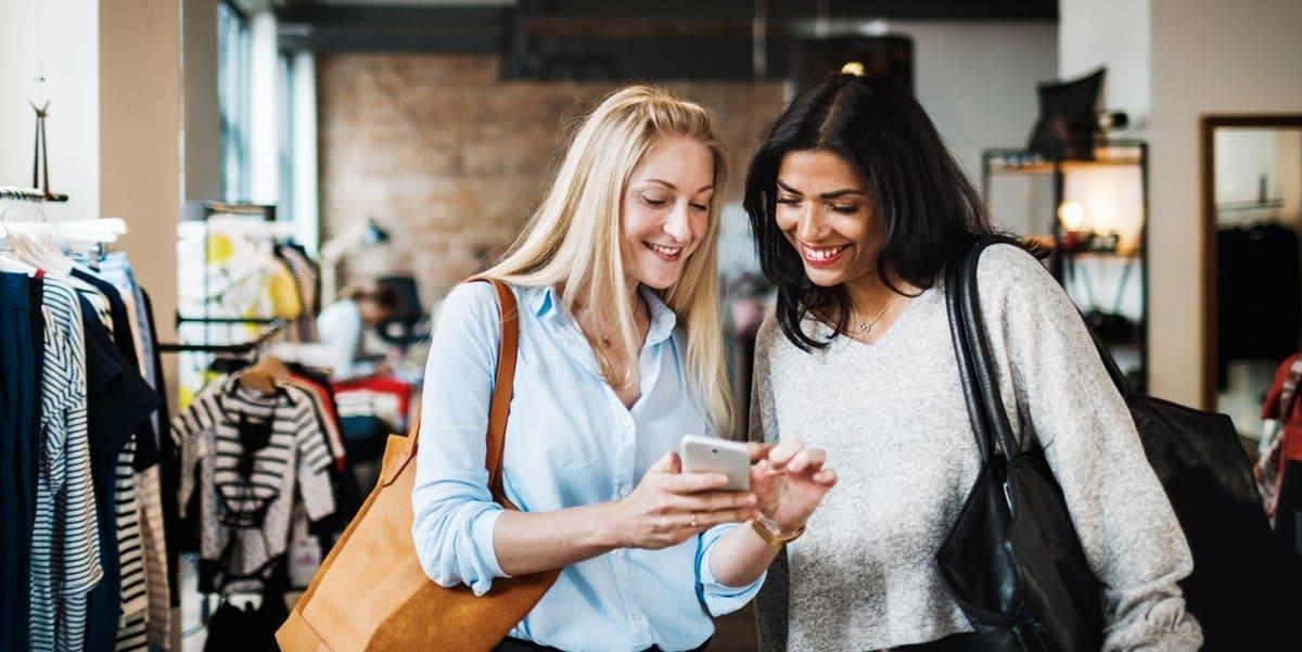 two women in retail setting, looking at phone